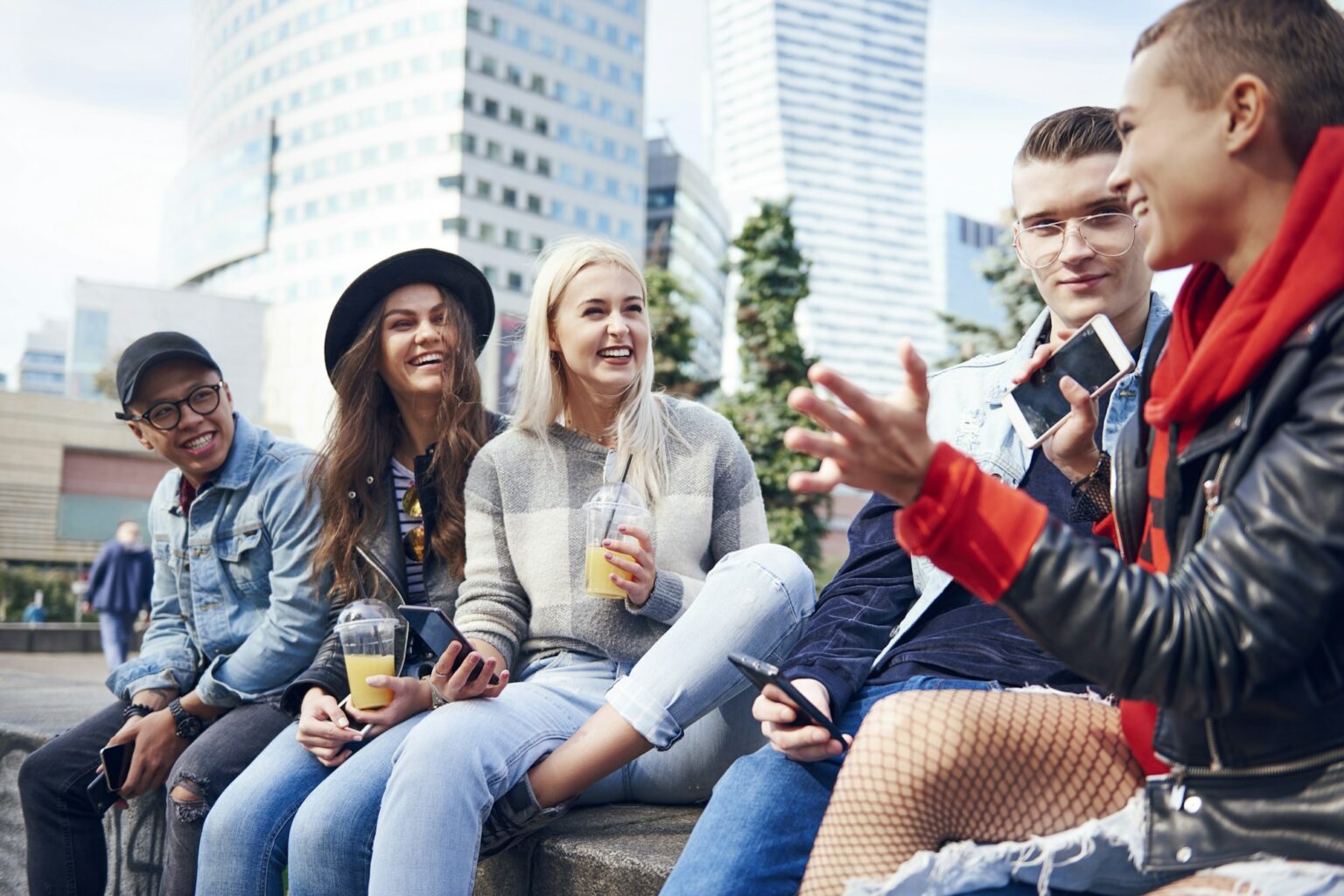 Five young adult friends sitting on wall chatting in city